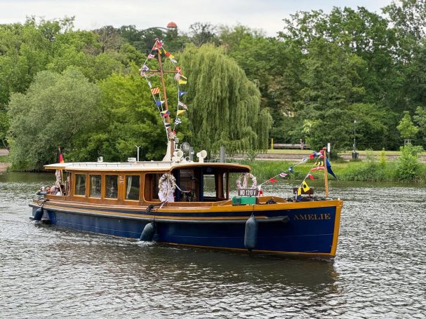 Ein bunt geschmücktes Boot fährt auf einem ruhigen Gewässer vorbei, umgeben von Bäumen.